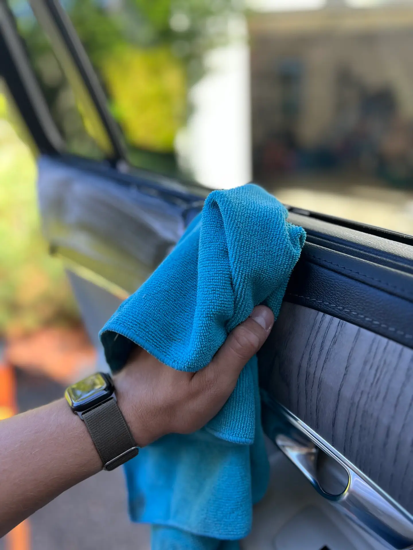 In the image, a person is meticulously wiping the interior surfaces of a car with a soft microfiber cloth. With focused attention, they glide the cloth over the dashboard, steering wheel, and center console, erasing dust and smudges with precision. The gentle motions reflect a commitment to achieving a spotless finish, enhancing the car's interior with a renewed shine.